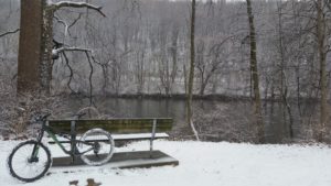 bike leans on a bench. with river and snowy woods in background